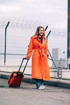 happy woman walking near airport, with luggage. Air travel, summer holiday. dressed in orange trench. Airport on a background