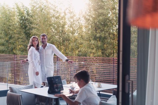 Happy elderly couple resting on the balcony of a luxury house while their son using a tablet. Selective focus. High-quality photo