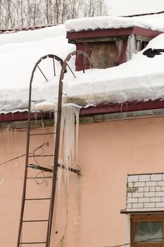 Long ice icicles hang from the edge of the roof. Against the background of the wall of an old brick house. Large cascades, even beautiful rows. Cloudy winter day, soft light.