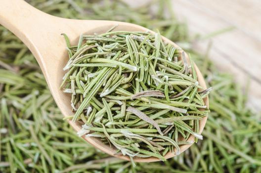 Dried rosemary spice in wooden spoon. Macro with shallow depth of field.