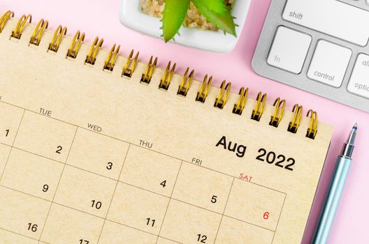 The August 2022 desk calendar with keyboard computer on pink background.