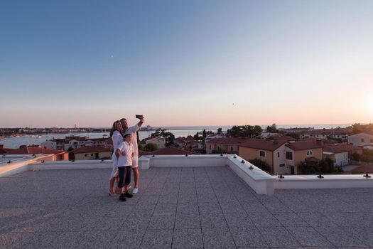 Happy family taking a selfie with a smartphone on the roof of their house at sunset. Selective focus. High-quality photo
