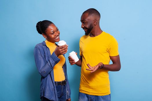 African american couple with cup of coffee enjoying romance in front of camera. People in relationship laughing and looking at each other. Boyfriend and girlfriend showing affection.