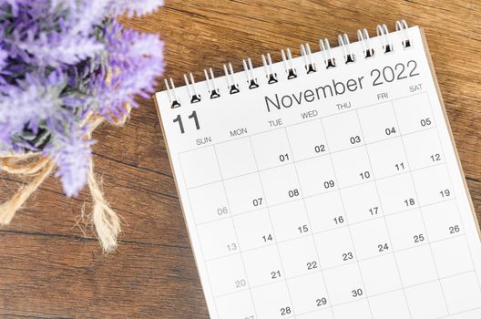 The November 2022 desk calendar with flower on wooden background.