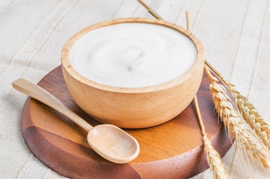 The Greek yogurt in a wooden bowl and dry barley on tablecloth.