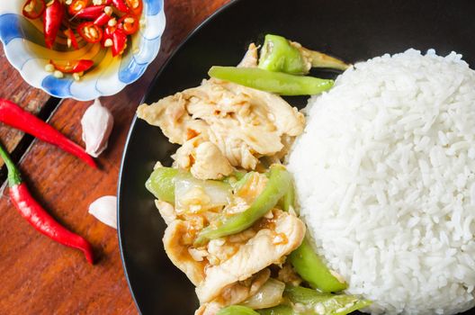 The Chicken stir fried with green chilli and steamed rice in black dish. Thai food.
