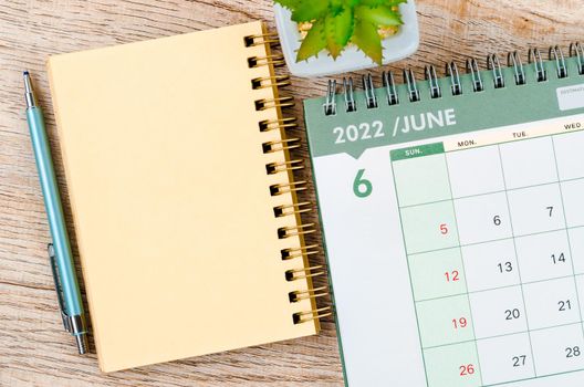 The June 2022 desk calendar and diary with small plant on wooden background.