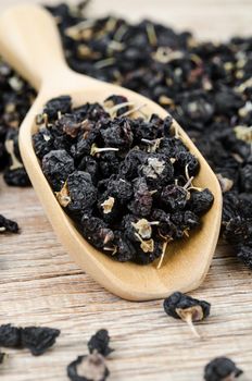 Black wolfberries or black goji berries, in a wooden spoon on table.