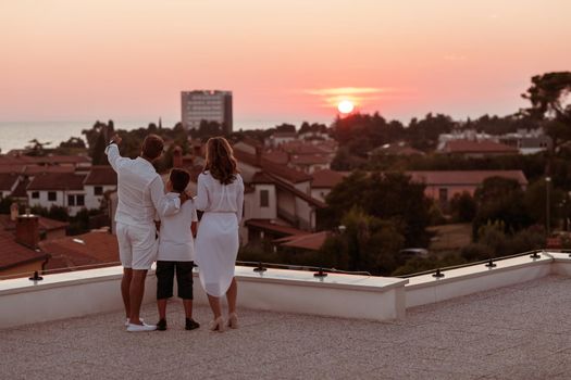 The happy family enjoys and spends time together on the roof of the house while watching the sunset on the open sea together. High-quality photo