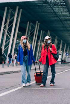 Two happy girls walking near airport, with luggage. Air travel, summer holiday