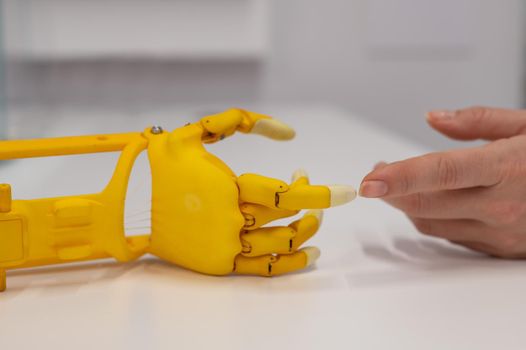 Woman's hand and a plastic hand prosthesis for a child on a white background