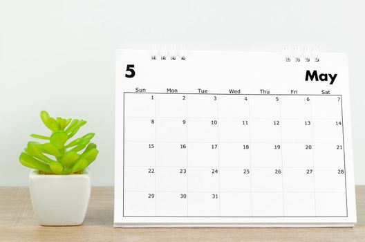 The May 2022 desk calendar with plant on wooden table.