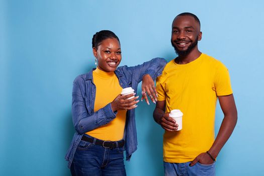 Cheerful couple in relationship holding cup of coffee in hand. Young people enjoying hot beverage, expressing love feelings and looking at camera. Girlfriend and boyfriend in studio.