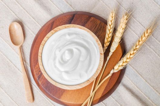 The Greek yogurt in a wooden bowl and dry barley on tablecloth.