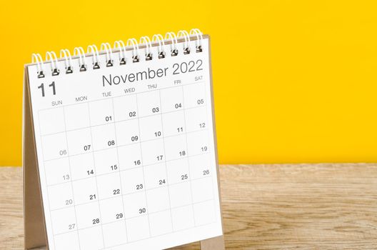 The November 2022 desk calendar on wooden table with yellow background.