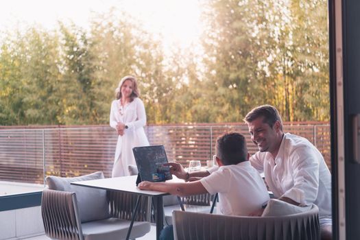 A happy elderly couple resting on the balcony of a luxury house, father and son using a tablet. Selective focus. High-quality photo