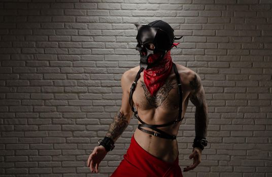 man with a naked torso in a bdsm demon mask with tattoos and leather belts and handcuffs