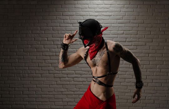 man with a naked torso in a bdsm demon mask with tattoos and leather belts and handcuffs