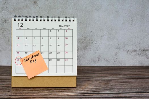December 2022 calendar on wooden desk with date circle and text on sticky note. Christmas Day on 25th December 2022