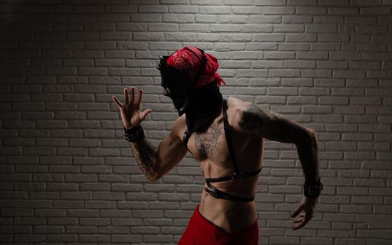 man with a naked torso in a bdsm demon mask with tattoos and leather belts and handcuffs