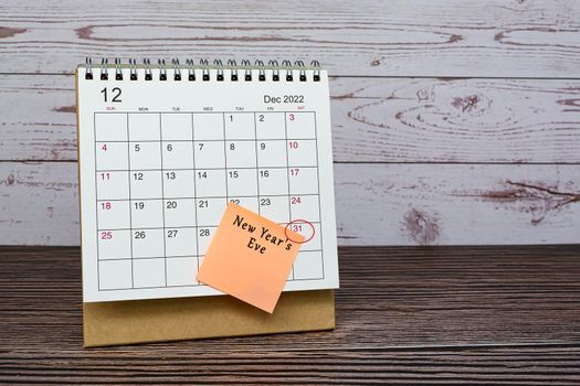 December 2022 calendar on wooden desk with date circle and text on sticky note. New year's eve on 31st December 2022.