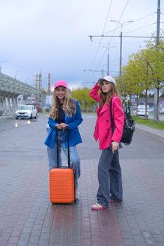 Two happy girls walking near airport, with luggage. Air travel, summer holiday.