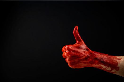 A woman's hand stained with blood shows a thumbs up on a black background