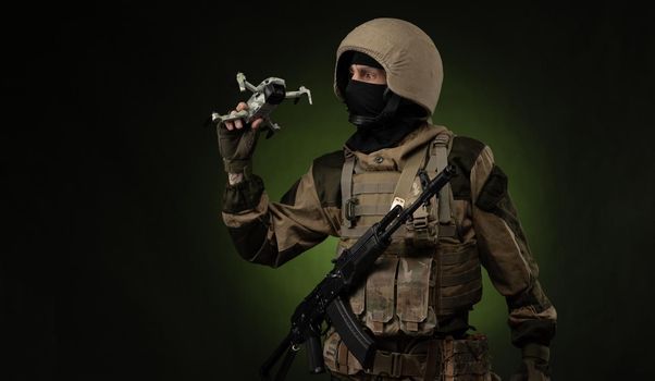 soldier in military clothes with a weapon launches a small unmanned quadcopter for reconnaissance on a dark background