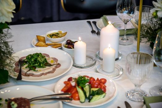 Wedding banquet. The festive table is served with plates with napkins and name cards, glasses and cutlery, and decorated with flower arrangements and candles.