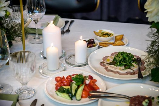 Wedding banquet. The festive table is served with plates with napkins and name cards, glasses and cutlery, and decorated with flower arrangements and candles.