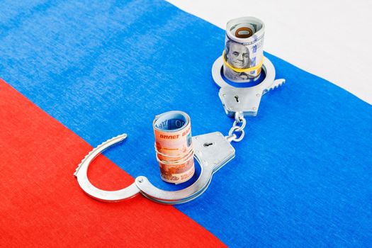 roll of us dollar banknotes in a handcuffs with a roll of russian ruble banknotes on flat full-frame russian flag background, closeup