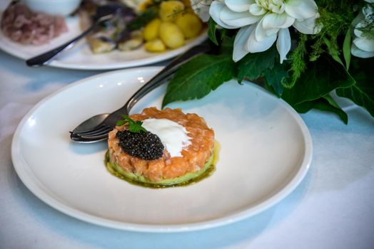 Fresh tartar with salmon, avocado and capers on white plate, close up.