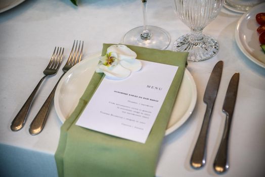 Wedding banquet. The festive table is served with plates with napkins and name cards, glasses and cutlery, and decorated with flower arrangements and candles.