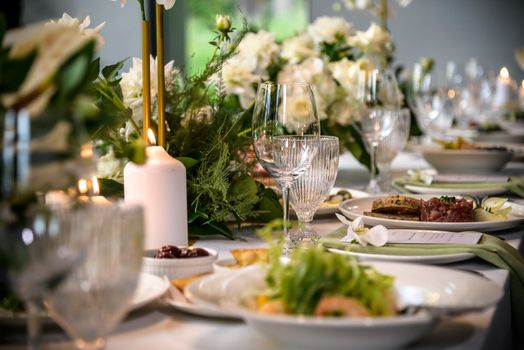 Wedding banquet. The festive table is served with plates with napkins and name cards, glasses and cutlery, and decorated with flower arrangements and candles.