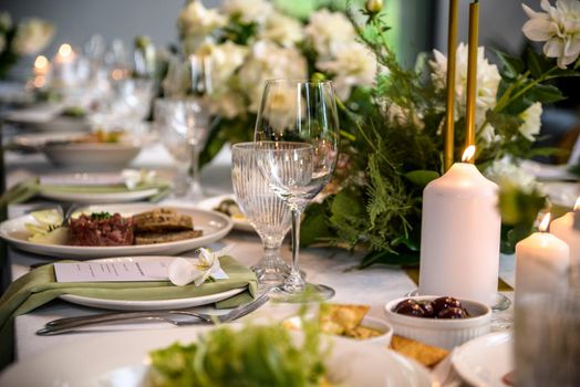 Wedding banquet. The festive table is served with plates with napkins and name cards, glasses and cutlery, and decorated with flower arrangements and candles.