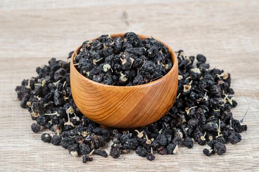 Black wolfberries or black goji berries, in a wooden bowl on table.