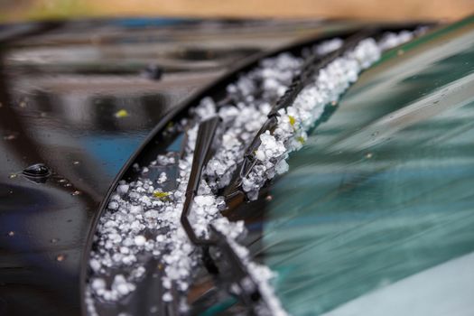 small hail ice balls on black car hood after heavy summer storm close-up with selective focus at daylight.