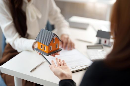 Real estate agents agree to sell a home and give small house model to clients at their agency's offices