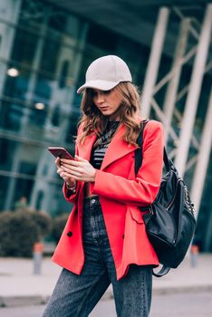 Stylish woman on the street uses a mobile phone. online shopping. use of mobile applications. beautiful woman with long dark hair in a red jacket, black top and a cap