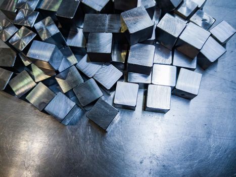 pile of small machined shiny steel cubes on metal surface, closeup with selective focus