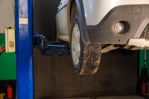 silver car lifted on elevator at maintenance in auto repair shop, close view