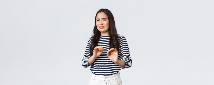 Lifestyle, beauty and fashion, people emotions concept. Reluctant and disgusted asian woman tell to stay away from her, step back and raising hands up defensive, grimacing from aversion and dislike.