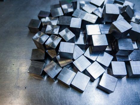 pile of small machined shiny steel cubes on metal surface, closeup with selective focus