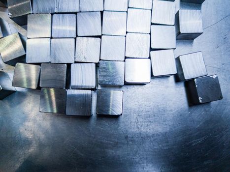 pile of small machined shiny steel cubes on metal surface, closeup with selective focus