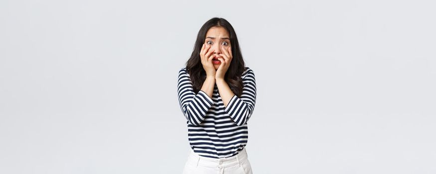 Lifestyle, people emotions and casual concept. Scared timid and insecure woman hold hands near mouth, screaming and looking terrified, shivering from fear, stand white background.