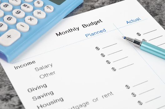 A print out of a monthly budget for your text with pen and calculator on wooden background.
