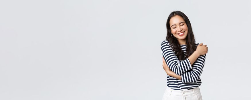 Lifestyle, people emotions and casual concept. Carefree smiling asian bodypositive girl close eyes and laughing carefree, embracing own body, love herself, white background.