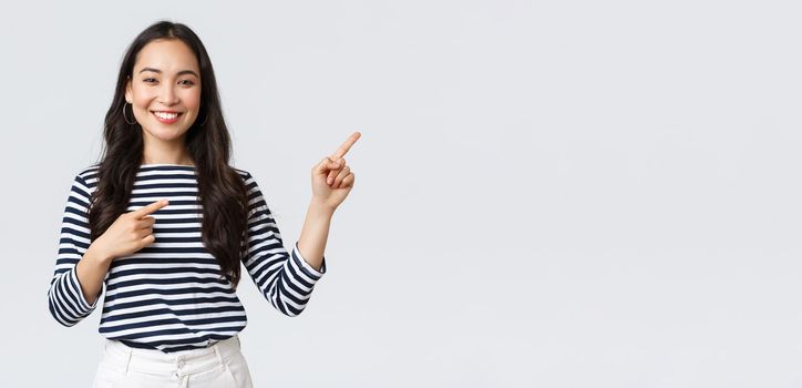 Lifestyle, beauty and fashion, people emotions concept. Good-looking young female in striped shirt pointing fingers right, inviting customers, advertise special discount, smiling at camera happy.
