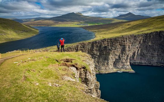 Rear view of unrecognizable tourists taking photos to Sorvagsvatn lake huge cliffs over the ocean, Faroe Islands