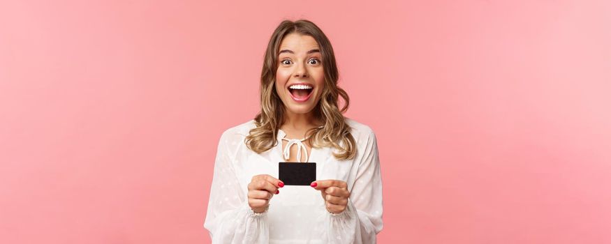 Close-up portrait of excited and happy good-looking blond female recommend bank, smiling amazed, holding credit card, paying for purchase, shopaholic in store feel upbeat.